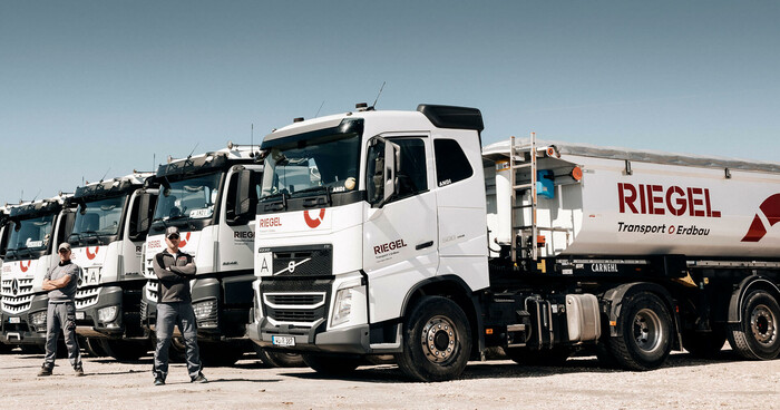 Lkw-Flotte von Riegel Erdbau mit Berufskraftfahrern davor, aufgereiht auf dem Firmengelände.
